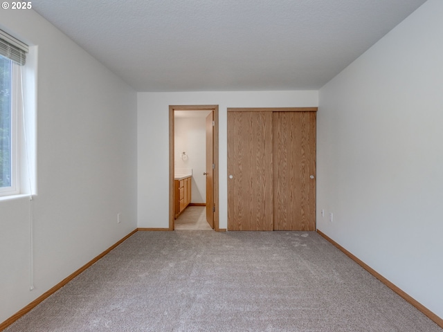 unfurnished bedroom featuring baseboards, connected bathroom, a closet, and light carpet
