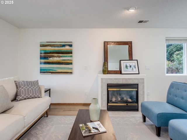 living area featuring baseboards, visible vents, a tiled fireplace, and wood finished floors