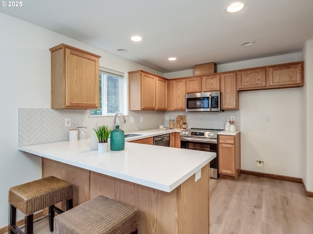 kitchen featuring a peninsula, tasteful backsplash, a sink, light wood-style flooring, and appliances with stainless steel finishes