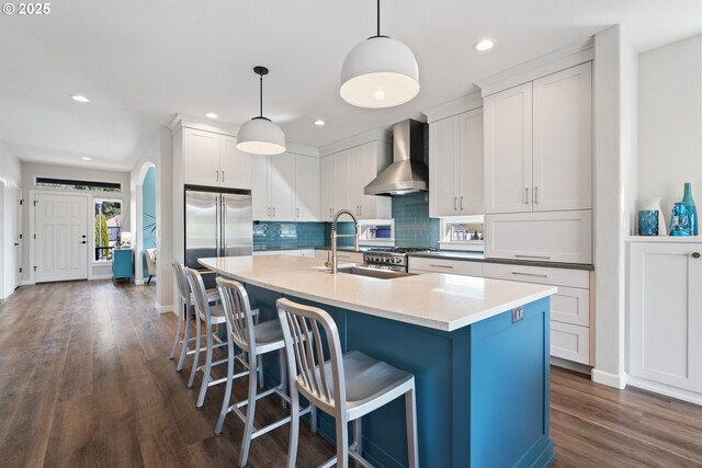 kitchen featuring wall chimney exhaust hood, high end appliances, dark wood-type flooring, backsplash, and a sink