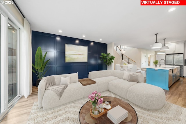 living room featuring light wood-style floors, a decorative wall, stairs, and recessed lighting