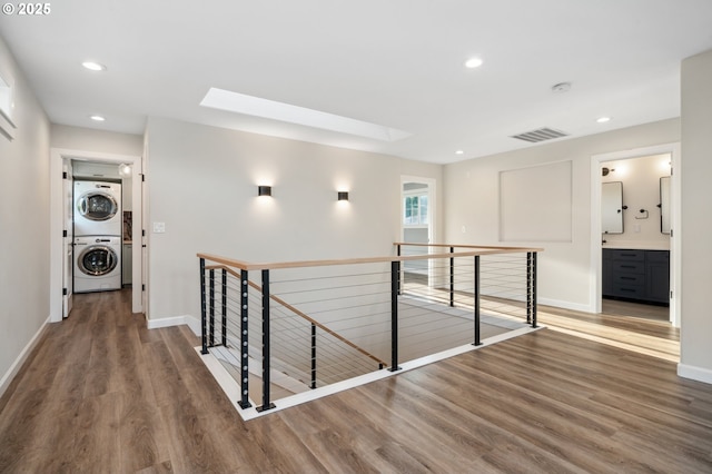 hall featuring an upstairs landing, stacked washer and clothes dryer, wood finished floors, a skylight, and baseboards