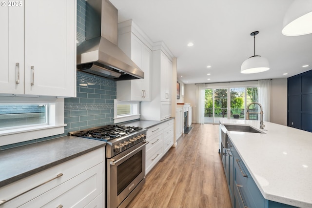 kitchen with high end stainless steel range, wall chimney range hood, light wood finished floors, white cabinetry, and tasteful backsplash