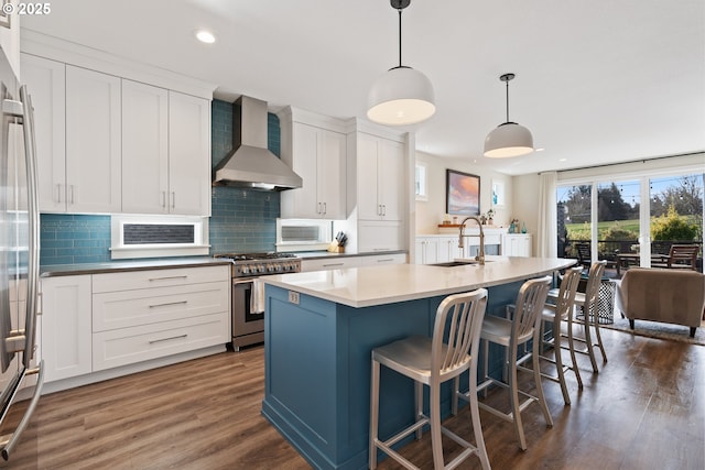 kitchen featuring wall chimney exhaust hood, appliances with stainless steel finishes, a sink, wood finished floors, and white cabinetry