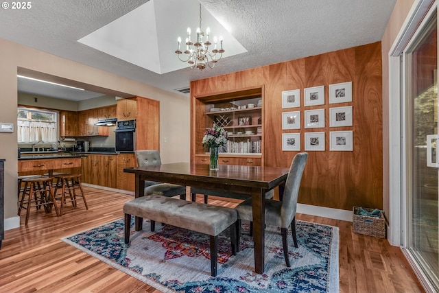 dining room featuring light wood-style floors, a textured ceiling, wooden walls, and an inviting chandelier