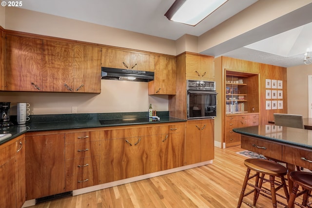 kitchen featuring black appliances, light wood-style floors, brown cabinets, and under cabinet range hood