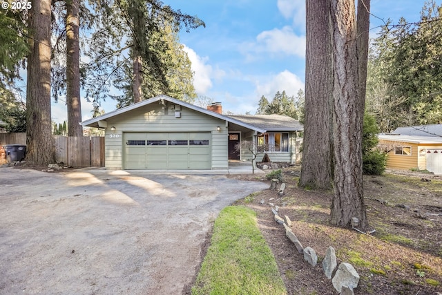 view of front of house featuring aphalt driveway, a chimney, an attached garage, and fence