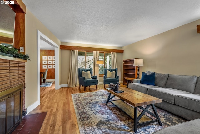 living room featuring a brick fireplace, a textured ceiling, baseboards, and wood finished floors