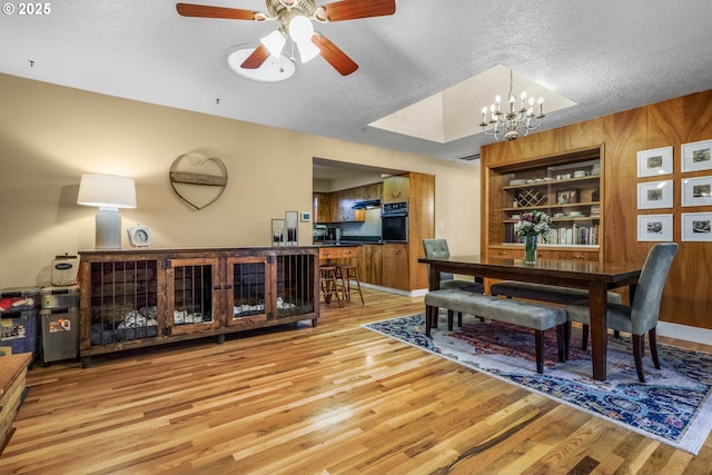 dining room featuring light wood-type flooring, wood walls, built in shelves, and a textured ceiling