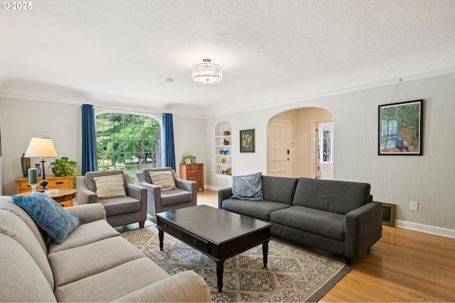 7150 SE 27th Ave, Portland, OR 97202 - living room with arched walkways, light wood-style flooring, a textured ceiling, built in features, and crown molding
