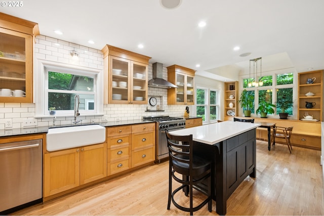 7150 SE 27th Ave, Portland, OR 97202 - kitchen featuring appliances with stainless steel finishes, wall chimney range hood, tasteful backsplash, light wood-style floors, and a kitchen island