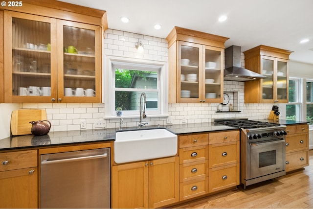 7150 SE 27th Ave, Portland, OR 97202 - kitchen featuring appliances with stainless steel finishes, wall chimney exhaust hood, tasteful backsplash, light wood-style flooring, and glass insert cabinets