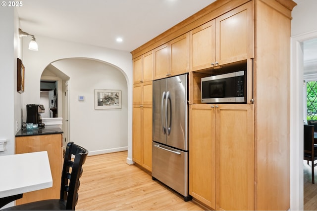 7150 SE 27th Ave, Portland, OR 97202 - kitchen with stainless steel appliances, light wood-style flooring, arched walkways, recessed lighting, and dark countertops