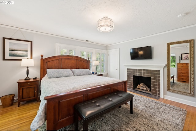 7150 SE 27th Ave, Portland, OR 97202 - bedroom featuring light wood-style flooring, a tile fireplace, multiple windows, a textured ceiling, and crown molding