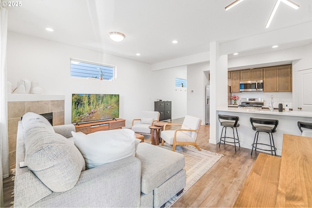 living area with light wood finished floors, a tiled fireplace, and recessed lighting