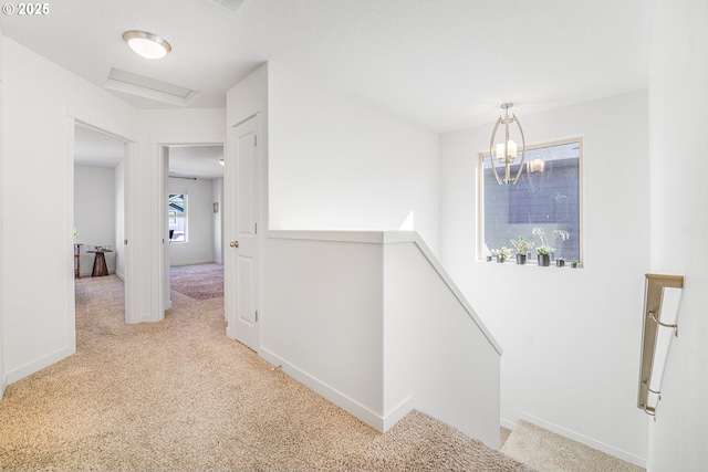 corridor featuring an inviting chandelier, attic access, carpet flooring, an upstairs landing, and baseboards