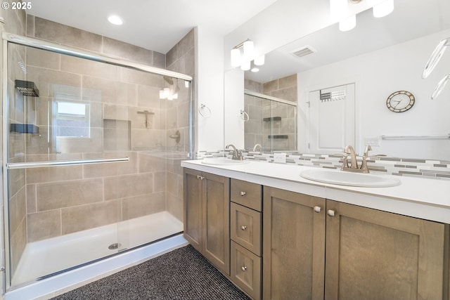 bathroom with double vanity, a shower stall, visible vents, and a sink