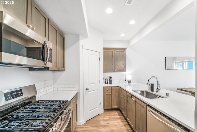 kitchen with light wood-style flooring, a peninsula, stainless steel appliances, light countertops, and a sink