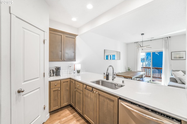 kitchen featuring light wood-style flooring, a peninsula, a sink, light countertops, and dishwasher