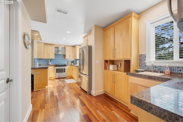 17460 Old Pacific Hwy, Rockaway Beach, OR 97136 - kitchen with stainless steel appliances, light brown cabinets, wall chimney exhaust hood, a sink, and light wood-type flooring