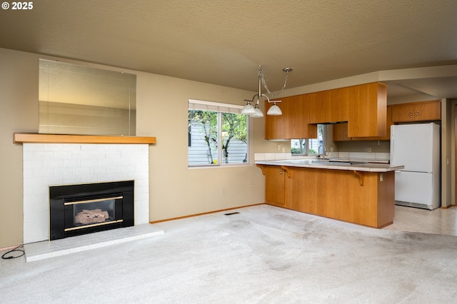 kitchen featuring a kitchen bar, decorative light fixtures, white refrigerator, kitchen peninsula, and light colored carpet