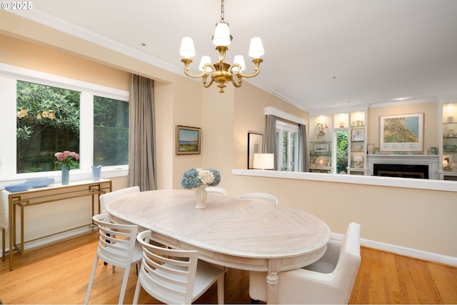dining room featuring a chandelier, healthy amount of natural light, crown molding, light wood finished floors, and a fireplace