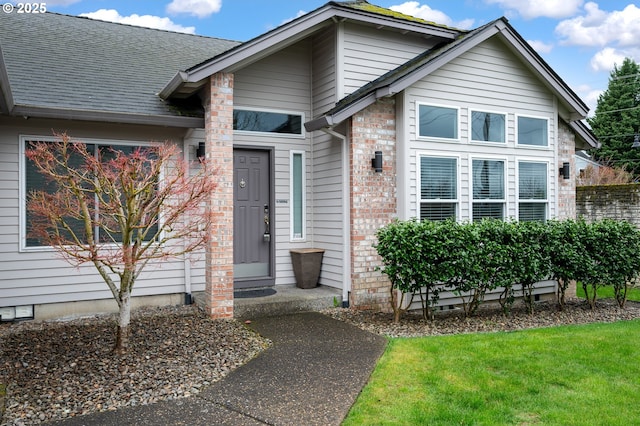 entrance to property with crawl space, brick siding, a yard, and a shingled roof