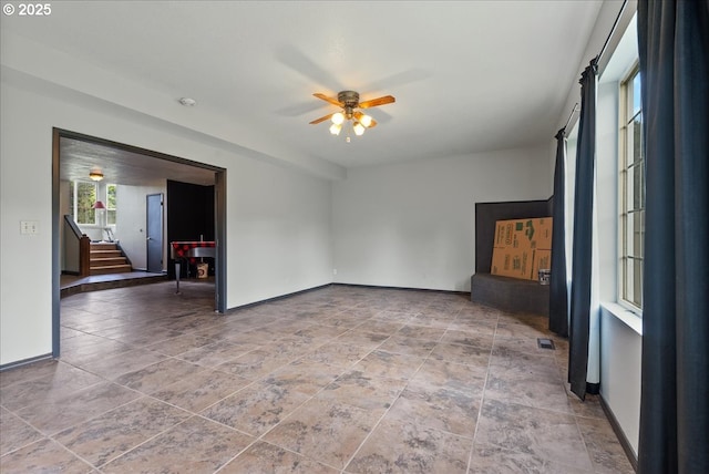 empty room with baseboards, a ceiling fan, and stairway