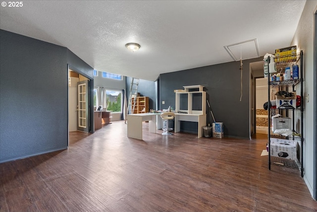 interior space featuring a textured ceiling, a textured wall, wood finished floors, and attic access