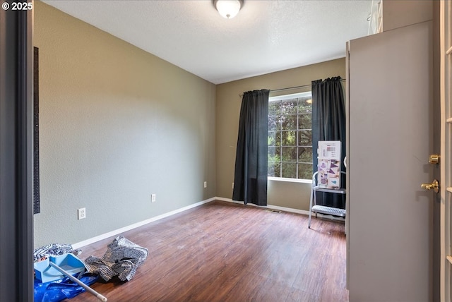 spare room featuring baseboards, a textured wall, and wood finished floors