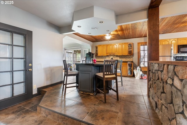kitchen with freestanding refrigerator, black microwave, stove, a breakfast bar area, and backsplash