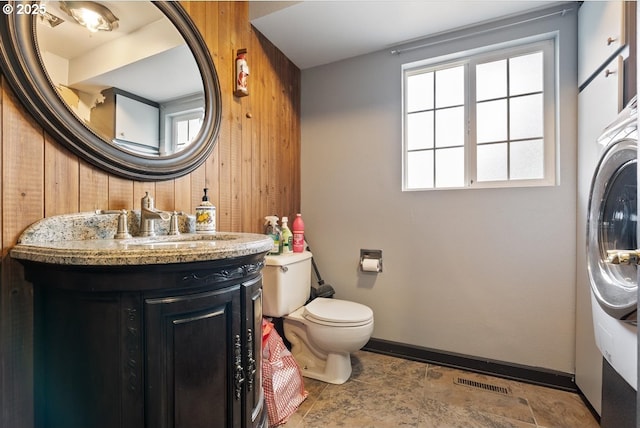 half bath featuring visible vents, vanity, baseboards, toilet, and wooden walls