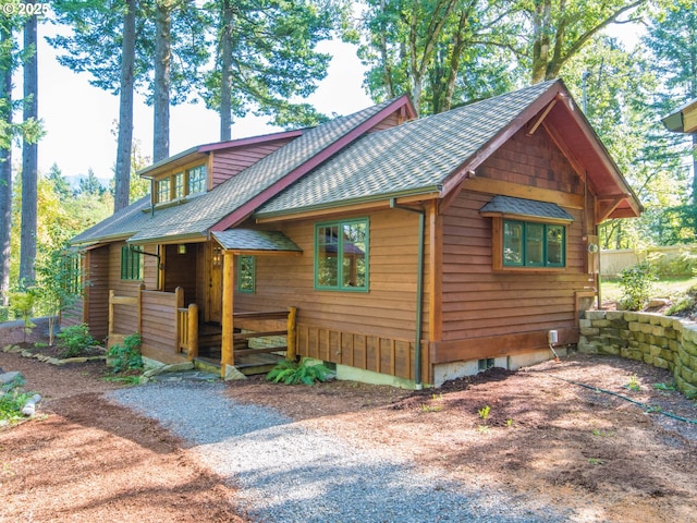 rustic home featuring gravel driveway and roof with shingles