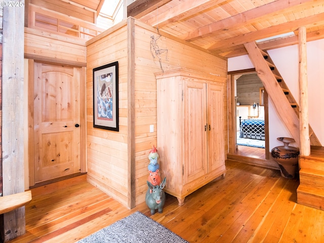 corridor featuring light wood-style floors, wooden walls, wood ceiling, and beamed ceiling