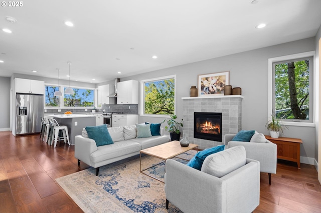 living area featuring recessed lighting, dark wood-style flooring, a glass covered fireplace, and baseboards
