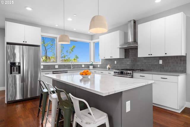 kitchen with wall chimney range hood, appliances with stainless steel finishes, a breakfast bar, and dark wood finished floors