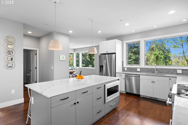 kitchen featuring dark wood-style flooring, light stone counters, a sink, appliances with stainless steel finishes, and backsplash