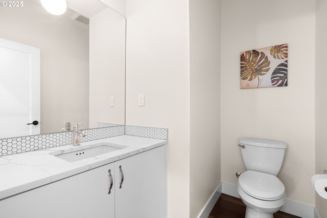 half bathroom with decorative backsplash, visible vents, baseboards, vanity, and toilet
