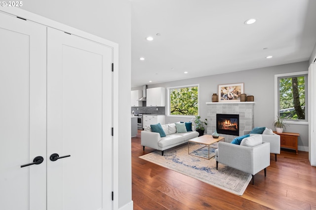 living area with recessed lighting, baseboards, a tiled fireplace, and wood finished floors