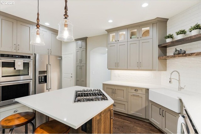 kitchen with decorative backsplash, a kitchen breakfast bar, appliances with stainless steel finishes, open shelves, and dark wood-style floors