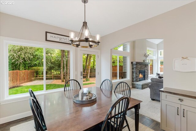 dining space featuring a notable chandelier, arched walkways, dark wood finished floors, a stone fireplace, and baseboards
