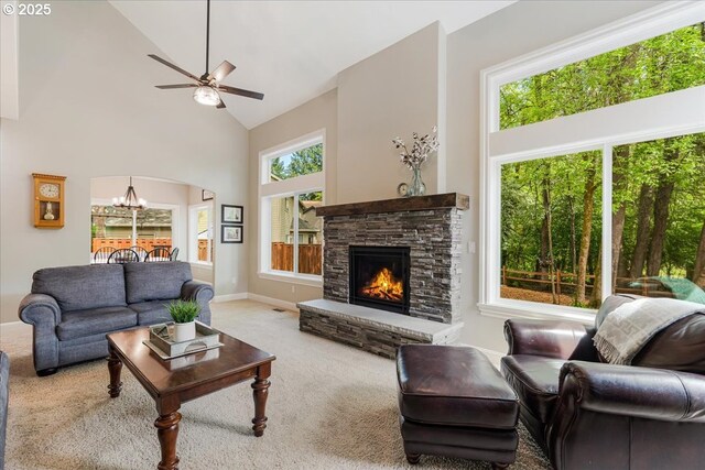carpeted living area featuring baseboards, a stone fireplace, high vaulted ceiling, arched walkways, and ceiling fan with notable chandelier