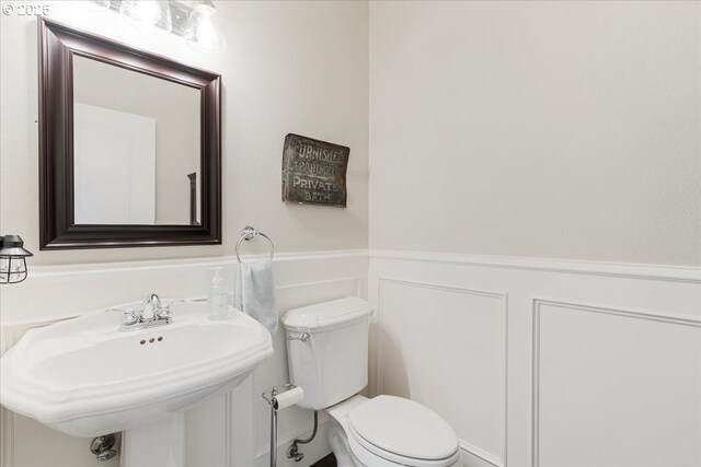 half bath featuring a decorative wall, toilet, a sink, and a wainscoted wall