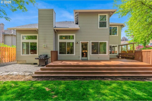 back of house with a chimney, a deck, fence, a yard, and a shingled roof