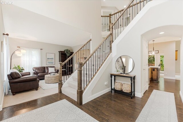 stairs with arched walkways, a high ceiling, recessed lighting, and wood finished floors