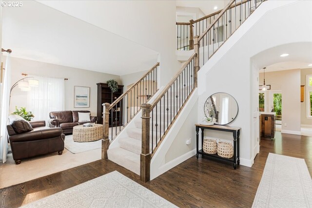 stairs featuring a high ceiling, arched walkways, recessed lighting, baseboards, and wood finished floors