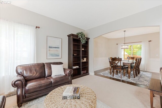 living room with carpet floors, arched walkways, a decorative wall, and a wainscoted wall
