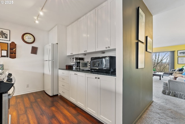 kitchen with black microwave, dark countertops, freestanding refrigerator, and white cabinets