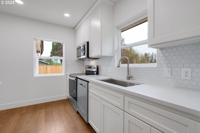 kitchen featuring white cabinets, appliances with stainless steel finishes, a sink, light wood-style floors, and light countertops