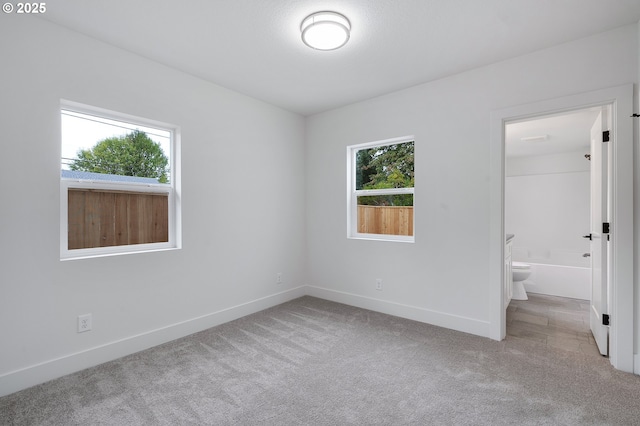 unfurnished bedroom featuring carpet floors, baseboards, and ensuite bath